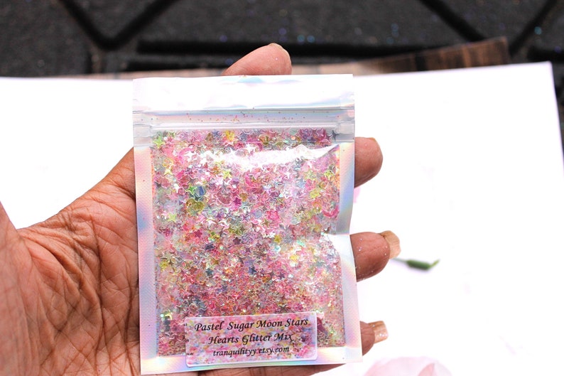 May include: A small clear plastic bag filled with pastel pink, blue, and green glitter stars and hearts. The bag has a label that reads "Pastel Sugar Moon Stars Hearts Glitter Mix tranquilitycrystals.com".