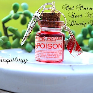May include: A miniature red poison bottle with a cork stopper and a silver cleaver charm. The bottle has a label that reads "CAUSTIC POTASH POISON". The background features green plants and the text "Red Poison Bottle Uped With A Bloody Hatchet".