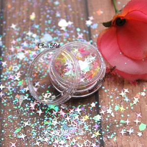 May include: A clear plastic jar filled with iridescent star-shaped glitter. The glitter is a mix of pastel colors, including pink, blue, green, and yellow. The jar is sitting on a wooden surface with a pink rose in the background. The text "Clear Pot" is visible on the jar.