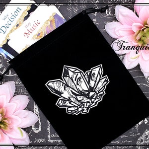 May include: A black velvet drawstring bag featuring a white crystal cluster design. The bag holds cards with the words "Wise Decision" and "Play Music". Pink flowers and the word "Tranquilityy" are in the background.