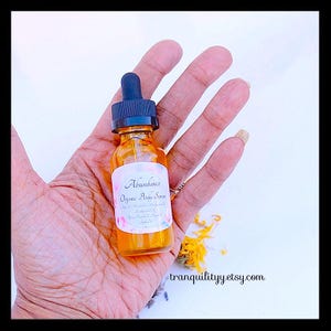 Pu&ograve; includere: Una piccola bottiglia di vetro ambrato con un contagocce nero, etichettata "Abundance Organic Body Serum". La bottiglia &egrave; tenuta in una mano aperta. Lo sfondo &egrave; chiaro con alcuni petali di fiori e l'indirizzo del sito web tranquilityyy.etsy.com.