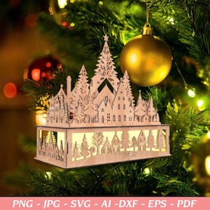 May include: A wooden Christmas village ornament with a star-topped tree design. The ornament is illuminated from within, showcasing a detailed cityscape of houses and trees. The ornament is hanging on a Christmas tree with gold and red ornaments.