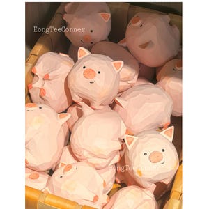 May include: A collection of light pink wooden pig figurines with carved details, including ears, snouts, and smiling faces. The pigs are nestled in a woven basket. The text "EongTeeConner" and "HongTeeConner" are visible.