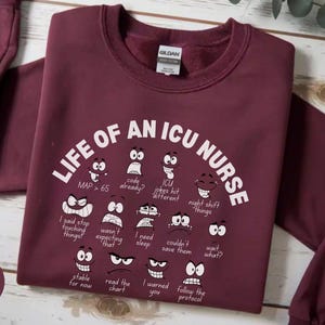 May include: Maroon crewneck sweatshirt with the text "LIFE OF AN ICU NURSE" and various cartoon faces expressing different emotions. The sweatshirt also has the word "maroon" printed on it.