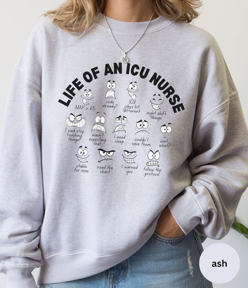 May include: Ash-colored sweatshirt with the text "LIFE OF AN ICU NURSE" in black. The design features cartoon faces with various expressions and phrases related to nursing, such as "MAP > 65" and "I need sleep."