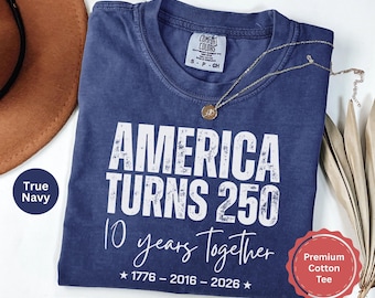 May include: A true navy blue short-sleeve t-shirt with white distressed text that reads America Turns 250, 10 years Together, and 1776 - 2016 - 2026 with two stars. The shirt features a Comfort Colors brand label at the inner neckline.