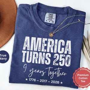 May include: A true navy blue short-sleeve t-shirt featuring white distressed text that reads AMERICA TURNS 250, 9 years Together, and 1776 - 2017 - 2026 with two stars. The shirt has a Comfort Colors brand label at the inner neckline indicating size S.