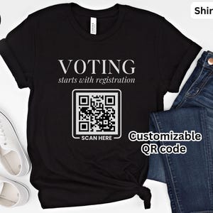 May include: A black t-shirt featuring the white text VOTING starts with registration above a square QR code graphic with the words SCAN HERE printed below it. The shirt is displayed alongside a pair of blue denim jeans and white sneakers.