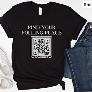 May include: Black t-shirt with the text "FIND YOUR POLLING PLACE" above a QR code and the words "SCAN HERE" below. The shirt is paired with blue jeans and white sneakers.