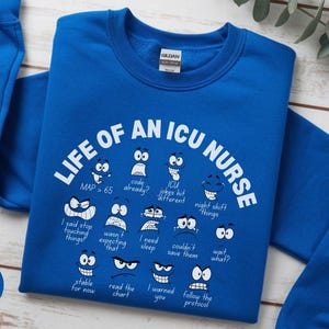 May include: Royal blue sweatshirt with the text "LIFE OF AN ICU NURSE" and various cartoon faces expressing different emotions. The sweatshirt also includes phrases like "MAP > 65" and "I need sleep."