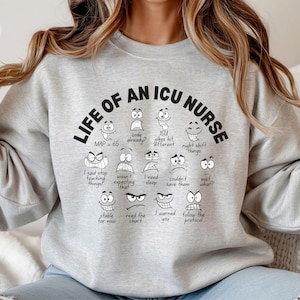 May include: A light gray sweatshirt with the text "LIFE OF AN ICU NURSE" in black. Below the text are various cartoon faces with different expressions and phrases like "code already?" and "night shift things".