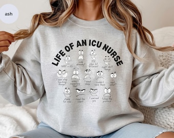 May include: A light gray sweatshirt with the text "LIFE OF AN ICU NURSE" in black. Below the text are various cartoon faces with different expressions and phrases like "code already?" and "night shift things".