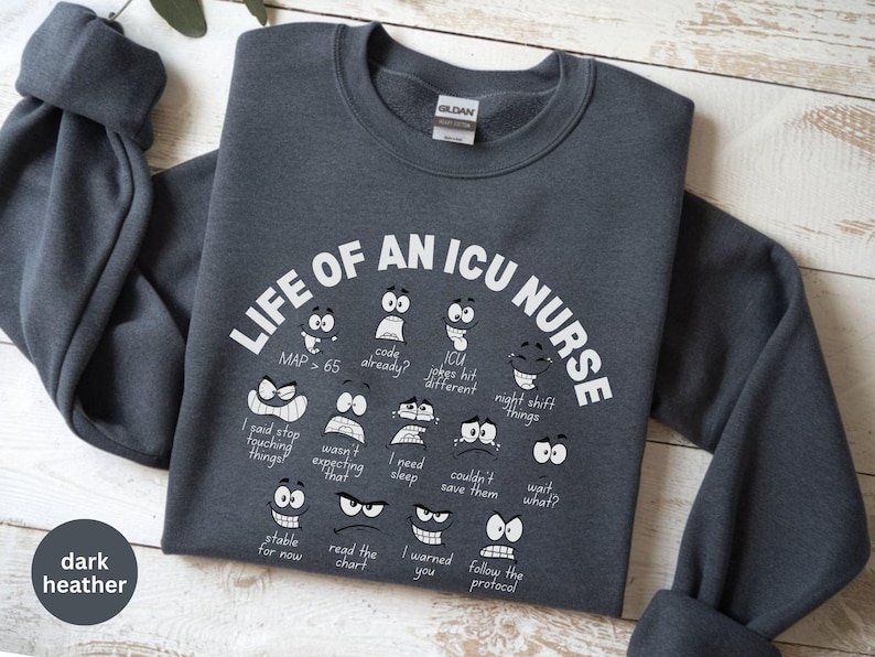 May include: Dark heather gray sweatshirt with the text "LIFE OF AN ICU NURSE" in white. The design includes various cartoon faces with phrases like "MAP > 65" and "night shift things".