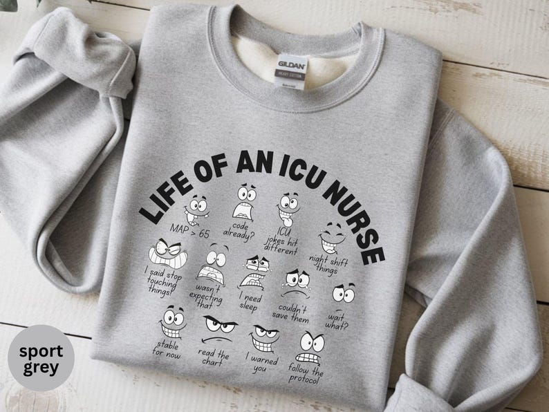 May include: Sport grey sweatshirt with the text "LIFE OF AN ICU NURSE" in black, with various cartoon faces and phrases. The sweatshirt is made of a soft material and has a crew neck.