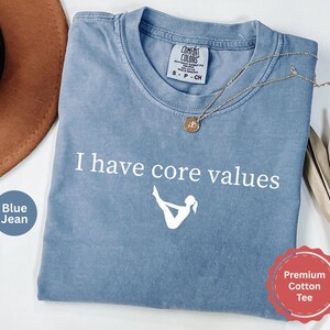 May include: A blue jean colored short-sleeve t-shirt with a crew neckline. The shirt features the white text I have core values above a white graphic of a person in a boat pose. A small tag inside the collar reads Comfort Colors size S.