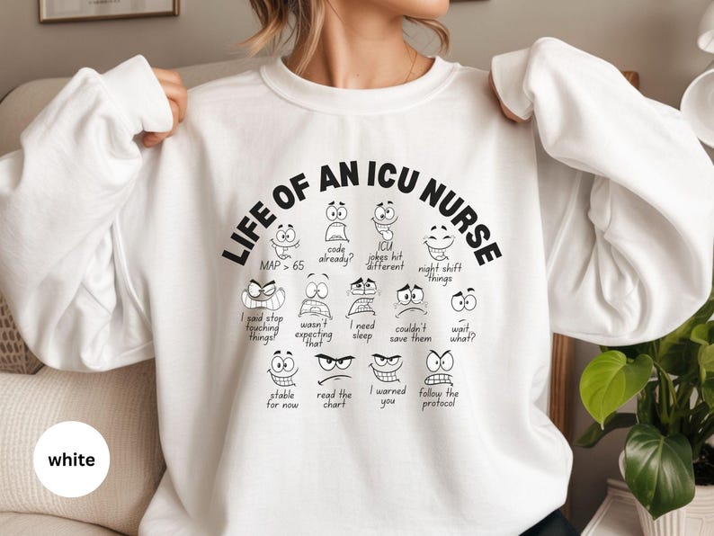 May include: White sweatshirt with the text "LIFE OF AN ICU NURSE" in black. The design includes various cartoon faces with expressions and phrases like "code already?" and "night shift things."