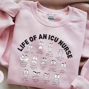 May include: Light pink sweatshirt with the text "LIFE OF AN ICU NURSE" in black, along with various cartoon faces expressing different emotions. The sweatshirt also features phrases like "MAP > 65" and "I need sleep."