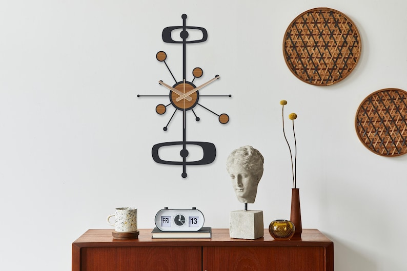 May include: A mid-century modern wall clock with a black frame and wooden accents hangs above a wooden cabinet. The clock features a starburst design with a circular wooden center. Other decor includes a bust, a flip clock, and woven wall hangings.