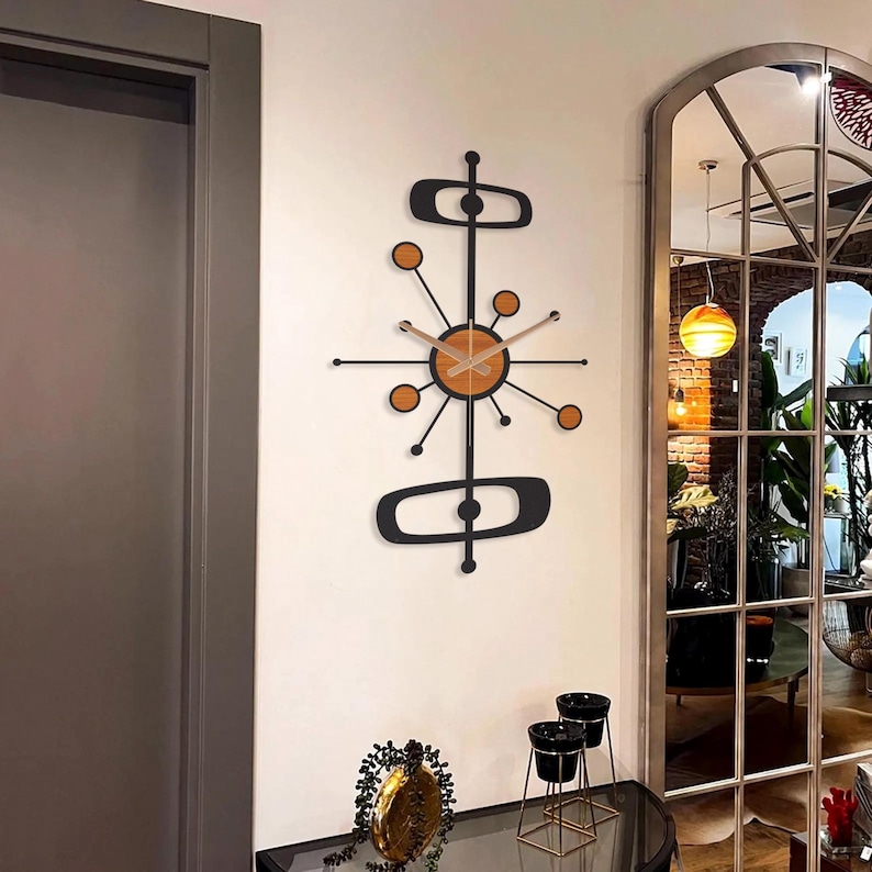 May include: A mid-century modern wall clock with a black frame and orange accents. The clock features a circular face with wooden hands and a unique starburst design. The clock is mounted on a white wall.