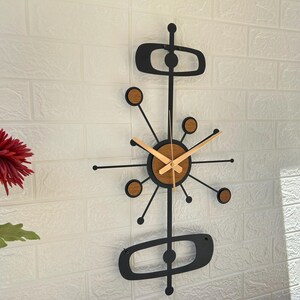 May include: A mid-century modern wall clock with a black metal frame and wooden accents. The clock features a circular face with wooden hands and a unique atomic design. The clock measures approximately 30 inches in height.