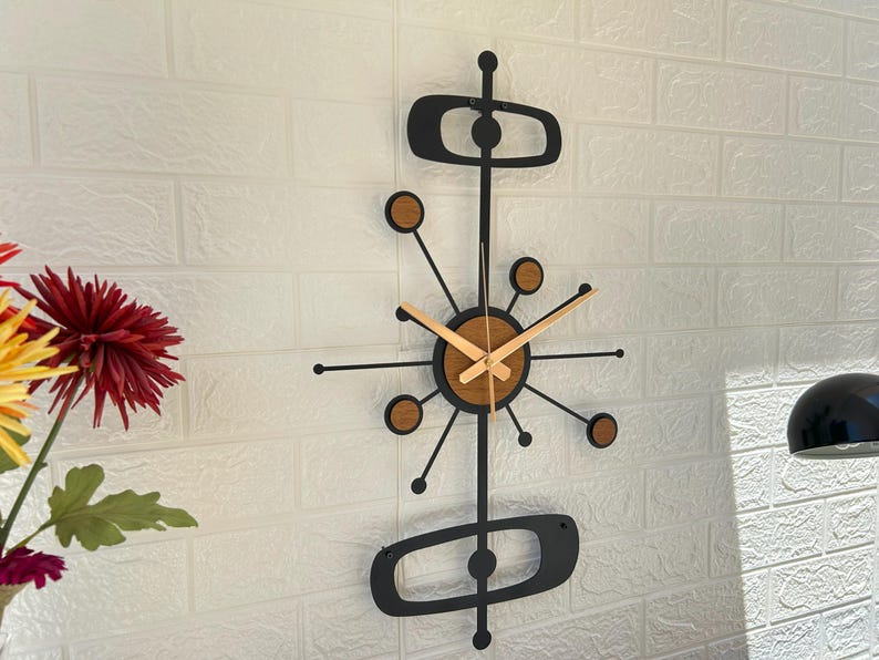 May include: A mid-century modern wall clock with a black metal frame and wooden accents. The clock features a circular face with wooden hands and a unique atomic design. The clock measures approximately 30 inches in height.