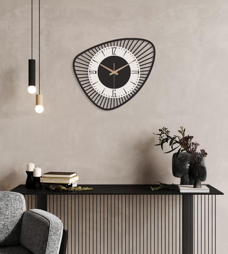 K&ouml;nnte beinhalten: Eine moderne Wanduhr in Schwarz und Wei&szlig; mit einer einzigartigen, asymmetrischen Form. Das Zifferblatt hat eine schwarze Mitte mit wei&szlig;en Ziffern und Zeigern. Die Uhr ist an einer neutralfarbenen Wand montiert, darunter dekorative Elemente.