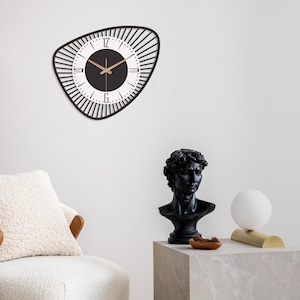 K&ouml;nnte beinhalten: Eine schwarz-wei&szlig;e Wanduhr mit einem einzigartigen, geometrischen Design. Die Uhr hat einen schwarzen Rahmen mit einer Reihe vertikaler Linien um das Zifferblatt. Das Zifferblatt ist wei&szlig; mit schwarzen Zahlen und Zeigern.