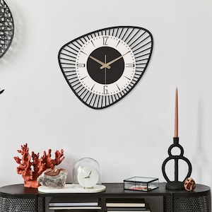 K&ouml;nnte beinhalten: Eine moderne Wanduhr in Schwarz und Wei&szlig; mit einer einzigartigen, asymmetrischen Form. Das Zifferblatt ist wei&szlig; mit schwarzen Ziffern und Zeigern. Die Uhr hat einen Durchmesser von ca. 50 cm und ist an einer wei&szlig;en Wand befestigt.