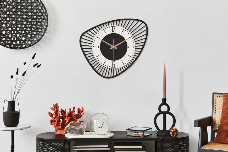 K&ouml;nnte beinhalten: Eine moderne Wanduhr in Schwarz und Wei&szlig; mit einer einzigartigen, asymmetrischen Form. Das Zifferblatt ist wei&szlig; mit schwarzen Ziffern und Zeigern. Die Uhr hat einen Durchmesser von ca. 50 cm und ist an einer wei&szlig;en Wand befestigt.