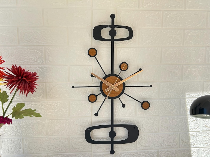 May include: A mid-century modern wall clock with a black metal frame and wooden accents. The clock features a circular face with wooden details and gold-colored hands. The design includes geometric shapes and a starburst pattern, adding a retro touch to any room.