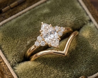 May include: A gold ring set featuring a central marquise-cut diamond flanked by three small round diamonds on each side, paired with a matching gold chevron-shaped wedding band. The rings are crafted from polished yellow gold metal.