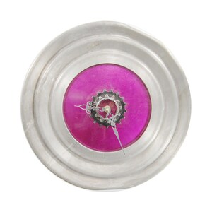 May include: A silver clock with a pink face and a gear-shaped clock hand. The clock is made from a repurposed metal object.