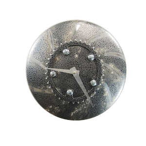May include: A round, silver-colored clock with a black face and a gear-shaped frame. The clock has a silver hour hand and a black minute hand.