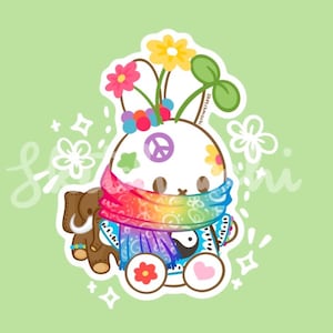 May include: A sticker illustration of a white round character wearing a rainbow-colored scarf, featuring a peace sign, a yin-yang symbol, and flowers on its head. A small brown elephant figure stands beside it, all set against a light green background.