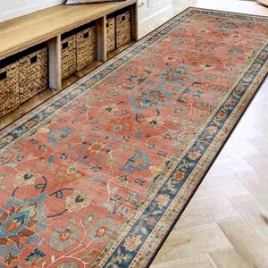 Può includere: Un lungo tappeto rettangolare con un motivo floreale nei toni del rosso, blu e beige. Il tappeto è posizionato su un pavimento in legno chiaro, che conduce a una porta aperta. Il design del tappeto include un bordo dettagliato.