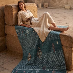 May include: A teal and blue patterned rug with diamond and geometric designs. The rug is rectangular and has a border. The rug is made of a soft material and is suitable for indoor use. The rug is placed on a stone surface.