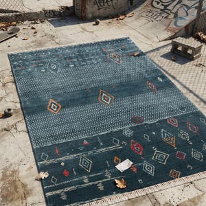 May include: A rectangular teal rug with geometric patterns, including diamonds and stripes in orange, red, and white. The rug has a fringed edge and is placed on a concrete surface, showcasing a modern design.
