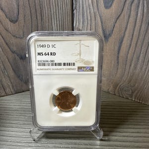 May include: A 1949 D 1C MS 64 RD penny in a clear protective case. The holder has a white insert with text and a Numismatic Guaranty Company logo. The penny is reddish-brown in colour.
