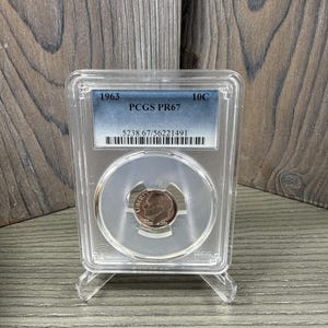 Può includere: Una moneta da 10C del 1963 in una custodia protettiva trasparente. La moneta è classificata PCGS PR67. La custodia ha un'etichetta con l'anno, il grado e il numero di serie. La moneta presenta un profilo di una persona.