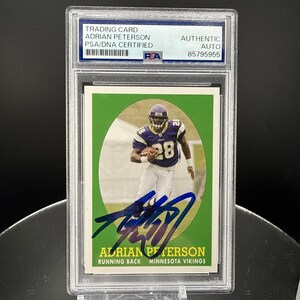 May include: A PSA/DNA certified trading card of Adrian Peterson, a Minnesota Vikings running back. The card features a player in a purple and white uniform holding a football, with a bold blue ink autograph across the bottom and the text ADRIAN PETERSON RUNNING BACK MINNESOTA VIKINGS.