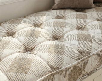 Puede incluir: Un cojín de asiento de ventana con un diseño acolchado. El cojín presenta un patrón de cuadros beige y blanco. Una almohada a juego descansa sobre el cojín. El cojín está cerca de una ventana.
