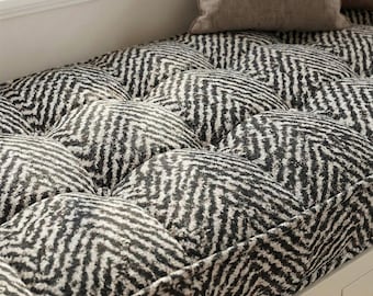 Puede incluir: Primer plano de un cojín de banco acolchado con un patrón de espiga en blanco y negro. El cojín está hecho de una tela suave y texturizada y está diseñado para brindar comodidad. El cojín forma parte de un asiento de ventana.