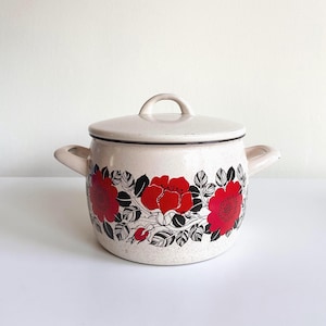 Puede incluir: Olla de esmalte color crema con tapa. La olla presenta un diseño floral de flores rojas y hojas negras. Tiene dos asas laterales y un asa de bucle en la tapa. Un artículo de menaje de cocina clásico.