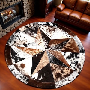 Puede incluir: Alfombra redonda de piel de vaca con diseño de estrella. La alfombra presenta un mosaico de piezas de piel de vaca marrón, negra y blanca. El patrón de estrella está centrado, con un borde marrón oscuro. La alfombra está sobre un suelo de madera.