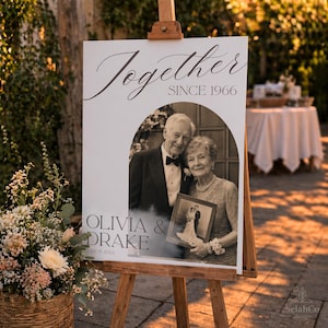 May include: A white rectangular wedding sign on a wooden easel featuring the text Together SINCE 1966 and OLIVIA & DRAKE JUNE 15 20XX. The sign displays a black and white photo of an older couple, with the person on the right holding a framed wedding photo.