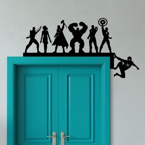 May include: Black silhouette door topper featuring superheroes, including a figure with a bow and arrow, a figure with a hammer, and the Hulk. Spider-Man is depicted hanging from the side. The topper is mounted above a teal door.