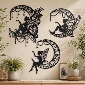 May include: Three black wall art pieces featuring silhouettes of winged figures sitting on ornate crescent moons. Each design incorporates intricate filigree patterns, hanging decorative elements, and detailed wings, creating a cohesive set of wall decor.
