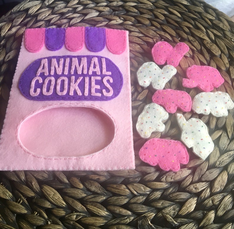 May include: A pink felt bag with a purple flap and the words "ANIMAL COOKIES" printed on it.  There are eight felt animal cookies in various colors and designs scattered around the bag.