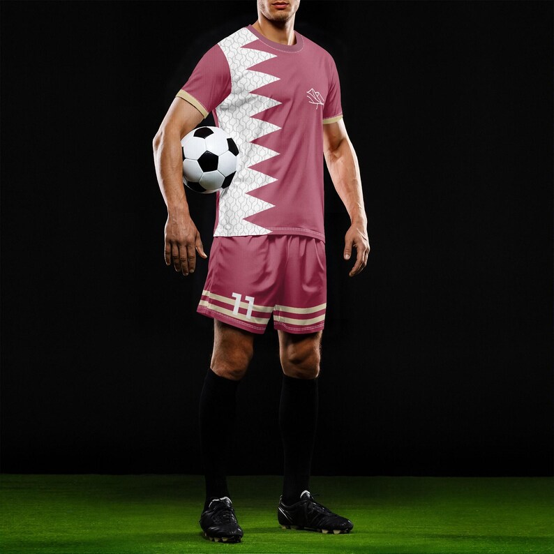 May include: A maroon soccer kit with a white and maroon geometric design. The jersey and shorts have beige accents. The shorts have the number 11. A black and white soccer ball is held. Black soccer cleats and socks complete the outfit.