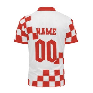 Op de afbeelding: Wit en rood voetbalshirt met de tekst "NAME" en het nummer "00" in rood. Het shirt heeft een rood-wit geblokt patroon op de mouwen en zijkanten. De kraag en manchetten zijn rood.